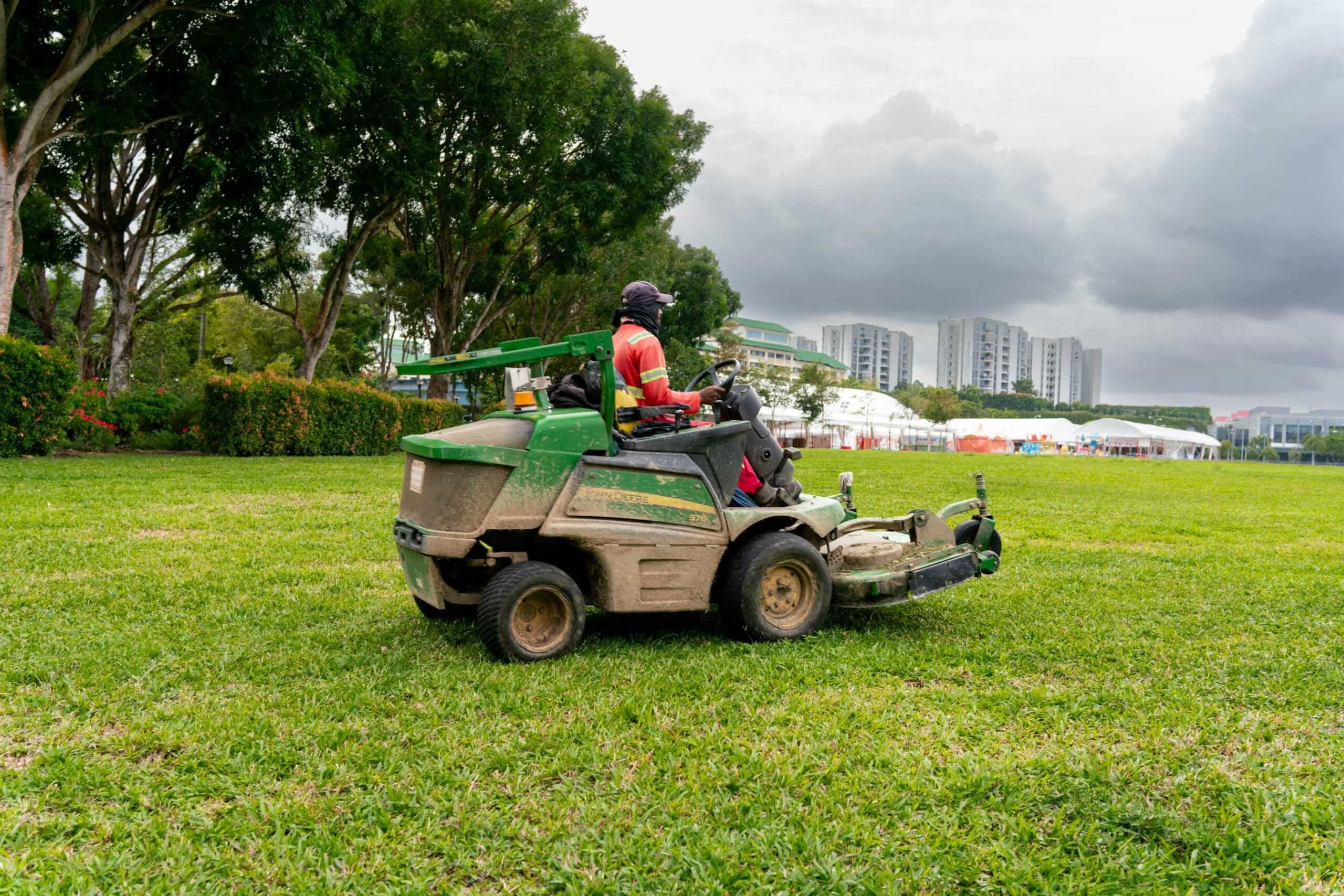 A professional landscaper operating a green commercial riding lawn mower across a vast public park turf field, seeking expert lawn care advice in Orlando, FL.
