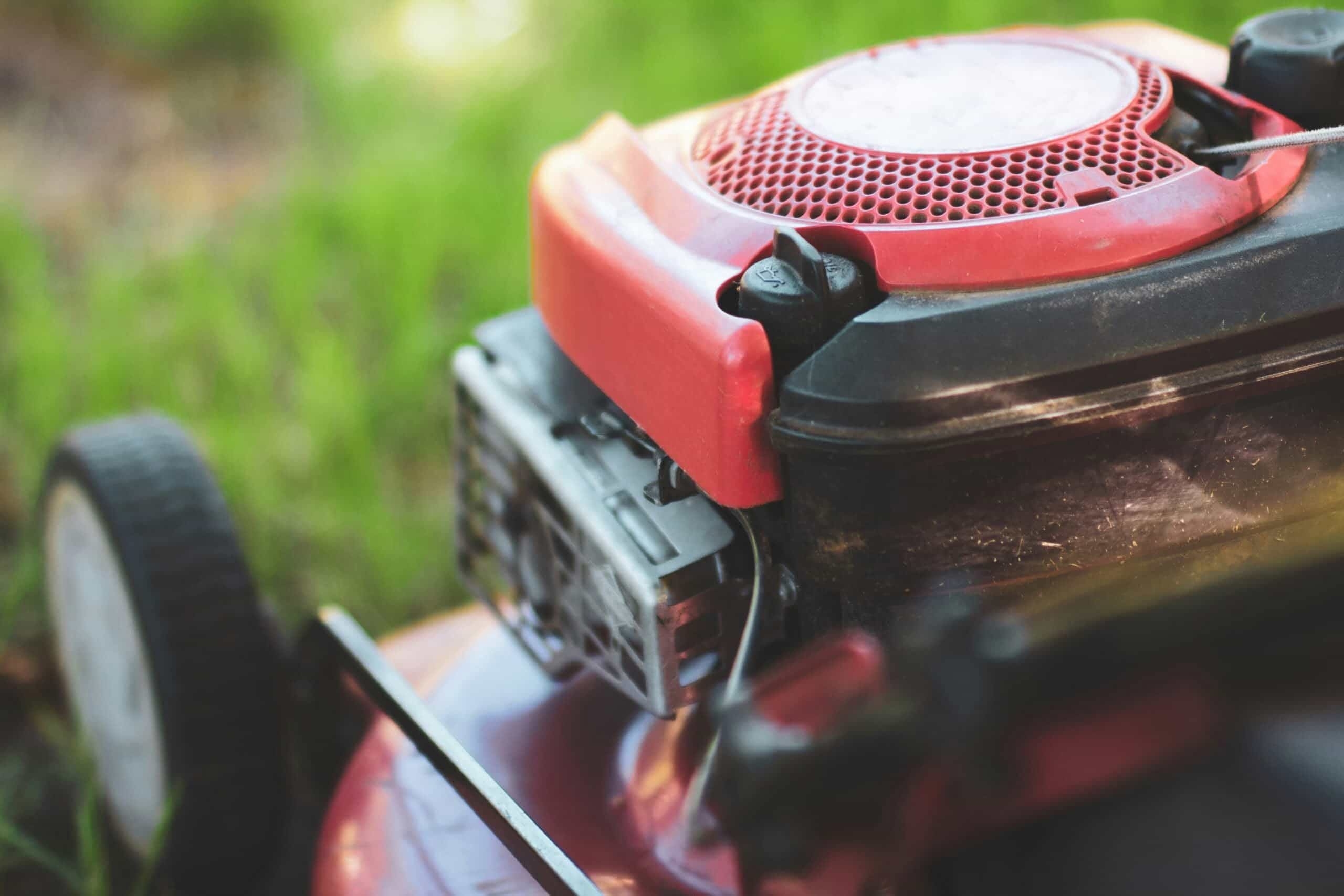 A close-up shot focusing on the red engine and pull-start assembly of a residential walk-behind lawn mower parked on green turf, ready for a grass cutting service near me in Austin, TX.