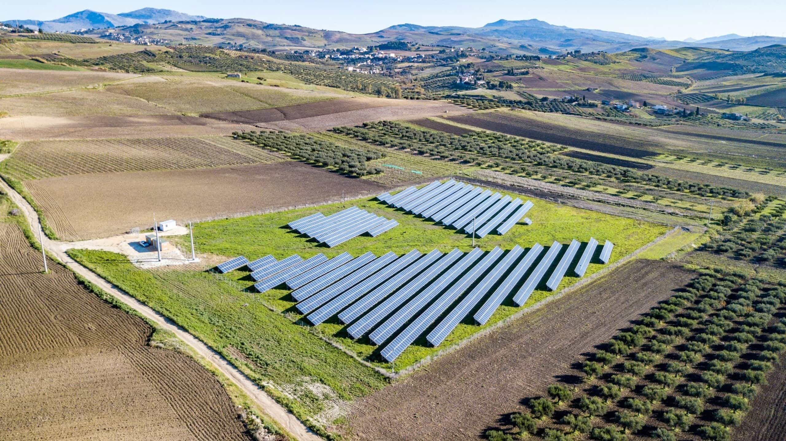 An aerial view of a large solar panel farm installation surrounded by agricultural plots, fields, and green landscaping requiring routine vegetation control and lawn care near me in Phoenix, AZ.